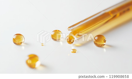 Several amber-colored droplets are scattered alongside glass pipettes on a clean, white surface, showcasing precise laboratory equipment used for liquid measurement and transfer 119908658