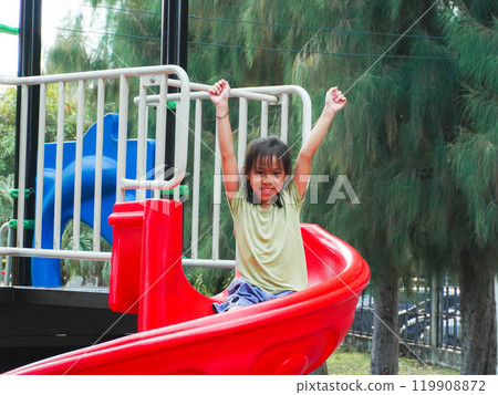 Children playing in the playground during summer vacation. Cute girl having fun on a colorful slide in an outdoor park. Children playing in the playground during summer vacation. Cute girl having fun on a colorful slide in an outdoor park. 119908872