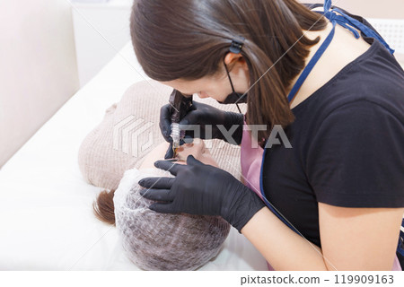 The master applies eyebrow makeup paint to the client with a tattoo machine. 119909163