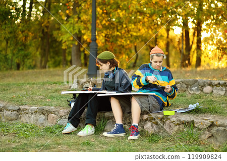 two young and innovative female artists conducting an outdoor painting lesson. Surrounded by nature, they are armed with easels, brushes, and a palette of colors, inspiring each other and their 119909824