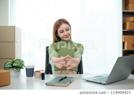 A woman is sitting at a desk with a laptop and a notebook 119909925