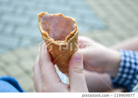 Ice cream cone in hand pastel gray background. . Concept of eating ice cream. A man holds a waffle without ice cream in his hand on a different light background. High quality photo 119909977