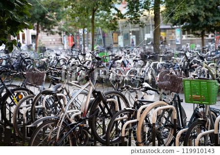A crowded urban bicycle parking area showcasing eco-friendly transportation in a city. Represents sustainability, urban biking culture, and minimalist lifestyle trends with greenery in the background. A crowded urban bicycle parking area showcasing eco-friendly transportation in a city. Represents sustainability, urban biking culture, and minimalist lifestyle trends with greenery in the background. 119910143