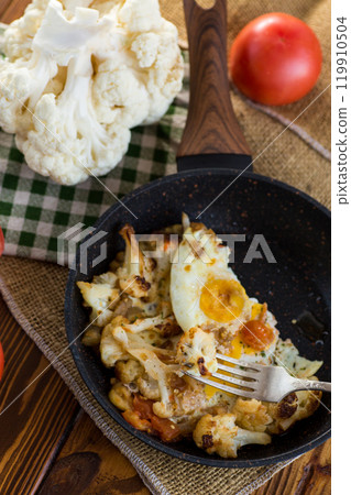 fried omelette with cauliflower and vegetables in a frying pan on a wooden table 119910504
