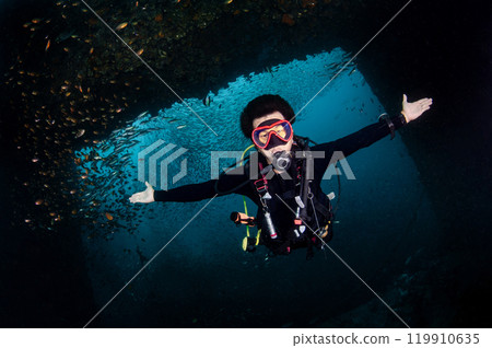 Male Scuba diver diving through a frame of wreck ship at King Cruiser wreck in Phuket, Thailand. Male Scuba diver diving through a frame of wreck ship at King Cruiser wreck in Phuket, Thailand. 119910635