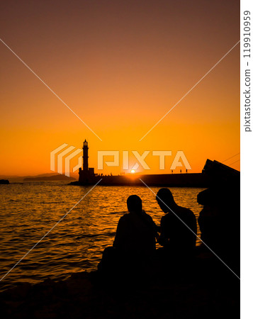 Lighthouse and silhouettes of people relaxing on the beach at sunset (Chania Old Town, Crete, Greece) Lighthouse and silhouettes of people relaxing on the beach at sunset (Chania Old Town, Crete, Greece) 119910959