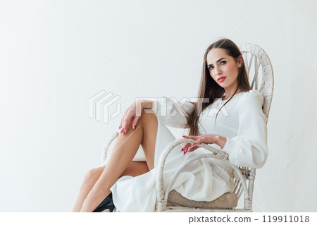 Beautiful woman in white summer dress sitting in armchair room 119911018