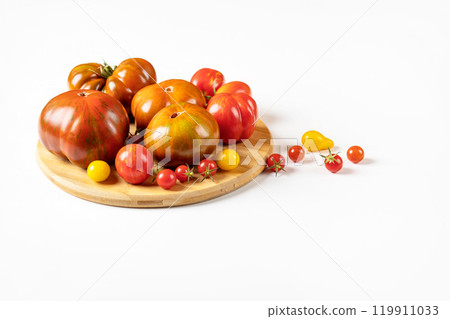 Red, green, yellow and striped tomatoes on a wooden cutting board on a light gray background with a place for text. Healthy food, fresh healthy vegetables from the garden 119911033