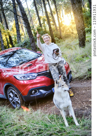 Woman taking pictures close to a car parked in a forest path. 119911931