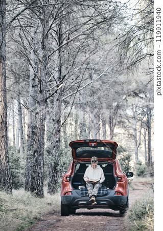 Woman reading a book in a car in a forest. Woman reading a book in a car in a forest. 119911940