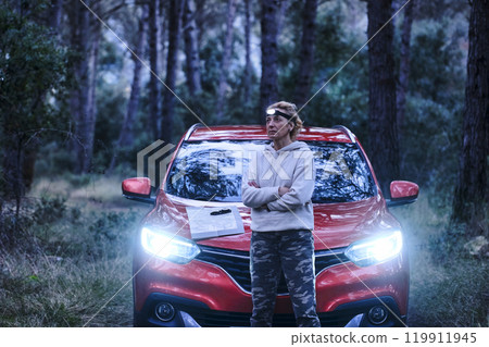 Car and adult woman lost in wooded area trying to orient herself at dusk. 119911945