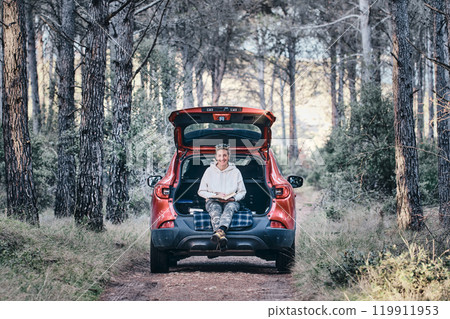 Woman reading a book in a car in a forest. Woman reading a book in a car in a forest. 119911953