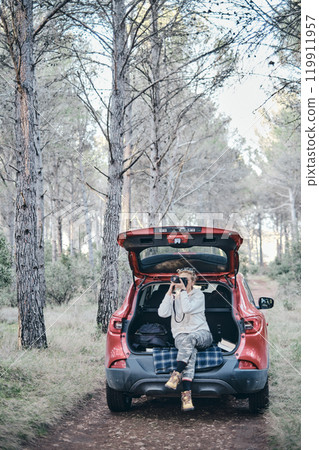Woman taking pictures close to a car parked in a forest path. Woman taking pictures close to a car parked in a forest path. 119911957