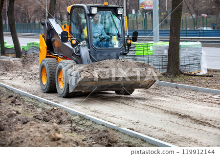 Skid steer loader moving soil, construction site machinery, urban development, dirt transportation, heavy equipment construction concept 119912144