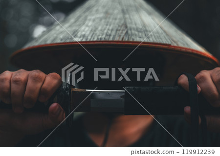 A determined samurai unsheathes his katana in a dark forest, representing honor and strength. Close-up of a courageous warrior slowly unsheathes his katana in front of his face. A determined samurai unsheathes his katana in a dark forest, representing honor and strength. Close-up of a courageous warrior slowly unsheathes his katana in front of his face. 119912239