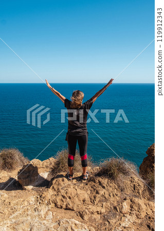 Girl standing on the edge of a cliff with outstretched arms Girl standing on the edge of a cliff with outstretched arms 119912343