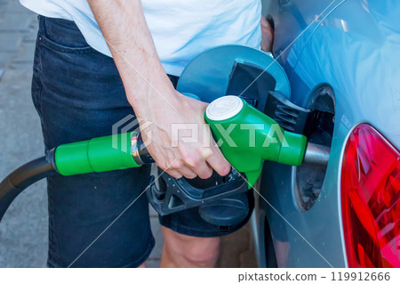 Refueling gun at the refuel station. Filling gun inserted into the hole of a gasoline tank of a car on a gasoline fueling. Close-up of the hand and fuel filling pistol. Refueling gun at the refuel station. Filling gun inserted into the hole of a gasoline tank of a car on a gasoline fueling. Close-up of the hand and fuel filling pistol. 119912666