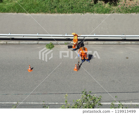 Unrecognized municipal cleaners manually sweep the city roadway. 119913499