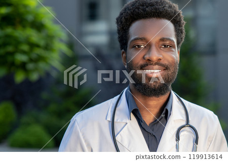 Male nurse standing outdoors wearing medical uniform and stethoscope near the hospital 119913614