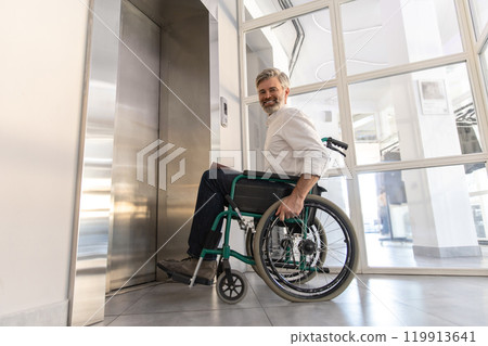Businessman in wheelchair in corporate office using touch panel to operate the lift 119913641