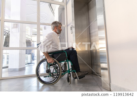 Male entrepreneur with disabilities in wheel chair waiting for elevator in office 119913642