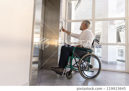Male entrepreneur with disabilities in wheel chair waiting for elevator in office 119913645