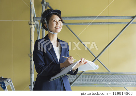 A woman in a suit looking at blueprints at the construction site 119914803