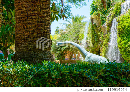 A dinosaur model in a park with flowing water 119914954