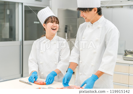 Male and female staff in chef coats preparing fish (cook, central kitchen, chef, vocational school, food processing) Male and female staff in chef coats preparing fish (cook, central kitchen, chef, vocational school, food processing) 119915142