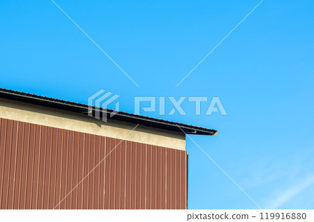 Brown metal sheet walls are attached to the concrete walls of a large factory. Brown metal sheet walls are attached to the concrete walls of a large factory. 119916880