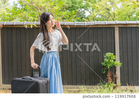 A young female traveler walking with a suitcase on the cobblestones in front of a black wall 119917608