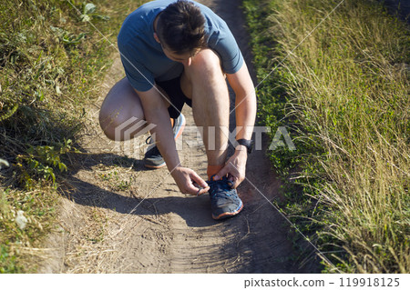 A young man ties the laces on his sneakers. A young man ties the laces on his sneakers. 119918125