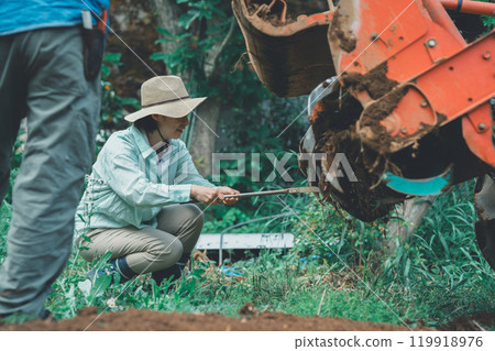 Farmer removing mud from tractor rotary 119918976
