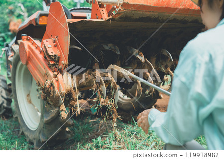 A woman removing mud from a tractor rotary A woman removing mud from a tractor rotary 119918982