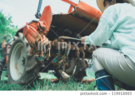 A young woman removing mud from a tractor rotary A young woman removing mud from a tractor rotary 119918983