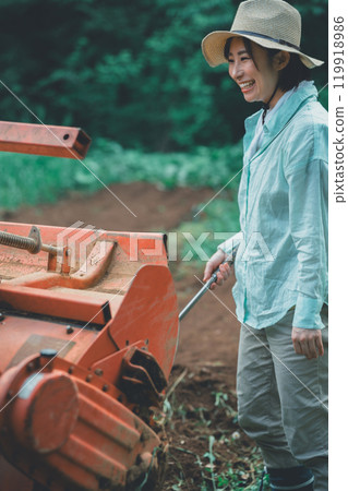 A woman removing soil from a tractor rotary A woman removing soil from a tractor rotary 119918986