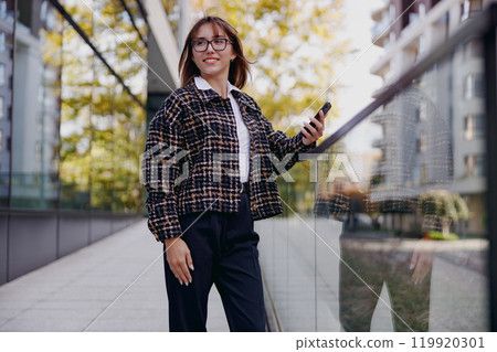 A Stylish Young Woman Holding a Phone in a Vibrant Urban Setting Filled with Life 119920301