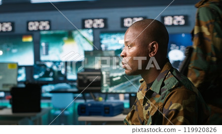 Portrait of military agent working in control room, analyzing aerial reconnaissance data. Intelligence corps agent controlling drones attacking strategic targets, camera A Portrait of military agent working in control room, analyzing aerial reconnaissance data. Intelligence corps agent controlling drones attacking strategic targets, camera A 119920826