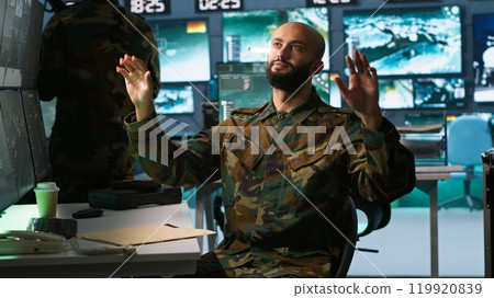Military agent using augmented reality tech in control room, analyzing aerial reconnaissance data. Intelligence corps expert controlling drones attacking strategic targets using AR hologram, camera A Military agent using augmented reality tech in control room, analyzing aerial reconnaissance data. Intelligence corps expert controlling drones attacking strategic targets using AR hologram, camera A 119920839