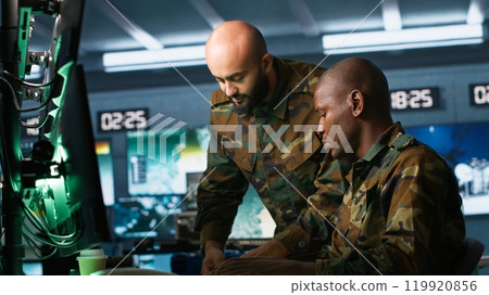 Soldier in military HQ base doing brainstorming with coworker, gathering information on enemy troops. Teamworking officers using tracking software to do assessment of enemy vulnerabilities, camera A 119920856