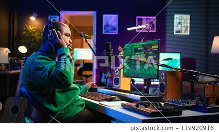 Professional artist writes new verses for a song in home studio, producing new music with mixing console and pc software. Composer works with audio equipment and tools, recording tunes. Camera B. 119920916