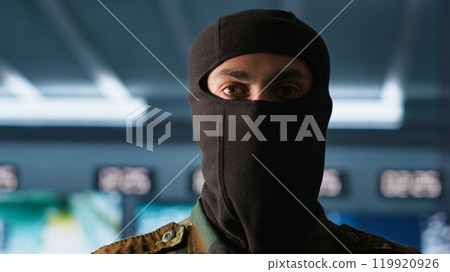 Portrait of terrorist loading gun, attacking enemy command center. Close up of masked insurgent reloading pistol during enemy base assault hijacking in guerilla warfare armed conflict, camera A 119920926