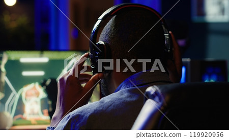 Man having fun playing videogames on PC while chatting with teammates. Excited gamer battling rival players, communicating with friends through headset microphone, camera A Man having fun playing videogames on PC while chatting with teammates. Excited gamer battling rival players, communicating with friends through headset microphone, camera A 119920956