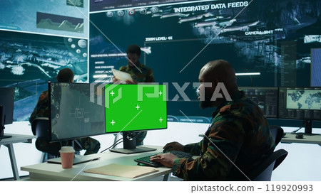 Soldier analyzing real time data next to green screen in high tech military office, processing intelligence for field operations and coordinating strategic missions to ensure national interests 119920993