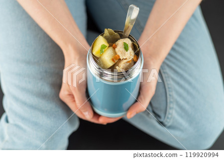 Food in a thermobox. Girl holds a thermos with food. Hot dish for the road. Food in a food thermos. View from above. 119920994