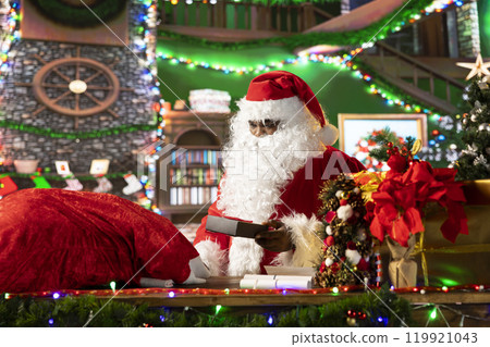 African american santa preparing his sack full of gifts in wrapping paper, delivering presents to wishful children around the world. Father Christmas decorating boxes with ribbons. African american santa preparing his sack full of gifts in wrapping paper, delivering presents to wishful children around the world. Father Christmas decorating boxes with ribbons. 119921043