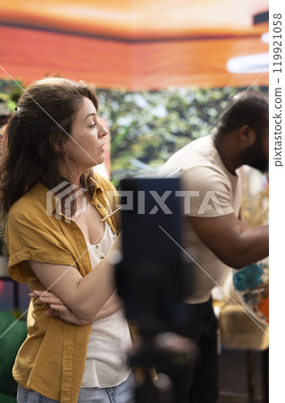Female artist explaining the painting techniques used on online tutorial, recording a vlog to teach people how to paint with watercolor on canvas. Team of painters filming in atelier. 119921058