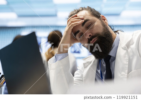 Frustrated and stressed specialist examining the test results for diagnostic, working under pressure to find the right treatment option. Professional medic worried while he checks hospital records. 119921151