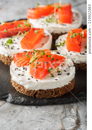 Canape sandwich with red fish, cream cheese, sesame and microgreens close-up on slate plate. Vertical 119922863