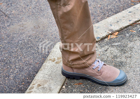 Male leg in brown beige trousers jeans and sports light easy shoes Male leg in brown beige trousers jeans and sports light easy shoes 119923427